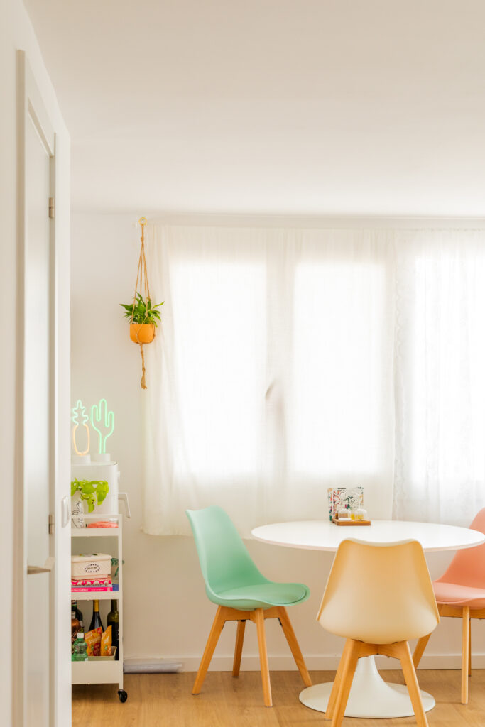 Comedor con sillas multicolores y ventana con cortinas